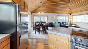 Une cuisine moderne avec des meubles en bois, un réfrigérateur en acier inoxydable, un coin repas avec une table et des chaises, et une grande fenêtre.