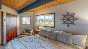 Un dormitorio con cama, techo de madera, decoración con timón de barco y ventana.