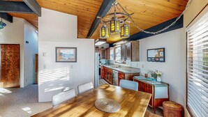 Un comedor con una mesa y sillas de madera, una lámpara colgante y una cocina al fondo.