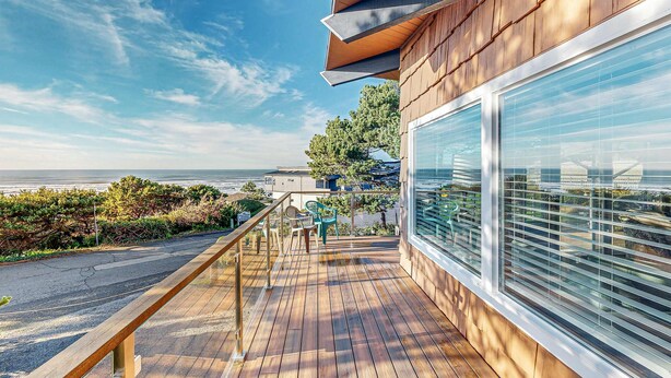 Una terraza de madera con barandilla, vista al océano y cielo despejado.