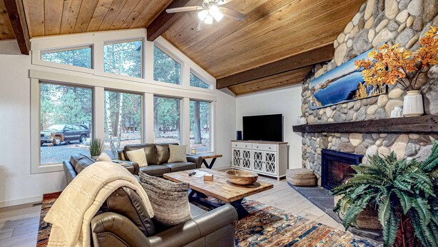 Ein Wohnzimmer mit Kamin aus Stein, einer Ledersofa und großen Fenstern mit Blick auf einen Wald.