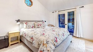 Ein Schlafzimmer mit einem Bett, einem Nachttisch, einem Sessel, einem Fenster und einer Tür zu einem Außenbereich.