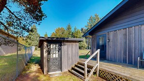 Eine Holzblockhütte mit einer kleinen Veranda und einer Tür, umgeben von einem Maschendrahtzaun und Bäumen.