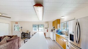 Eine moderne Küche mit Edelstahlgeräten, ein Essbereich mit einem langen Tisch und ein Wohnbereich mit einer Couch.