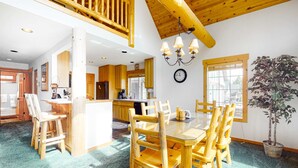 A spacious kitchen with wooden cabinets, a dining area with a wooden table and chairs, a chandelier, and a potted plant. - Inviting chalet with private hot tub, grill, 3 pools, hot tub, gym, & tennis (Eagle Crest)