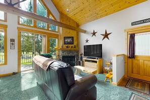 A spacious living room with a fireplace, a television, and a large window overlooking a forest.