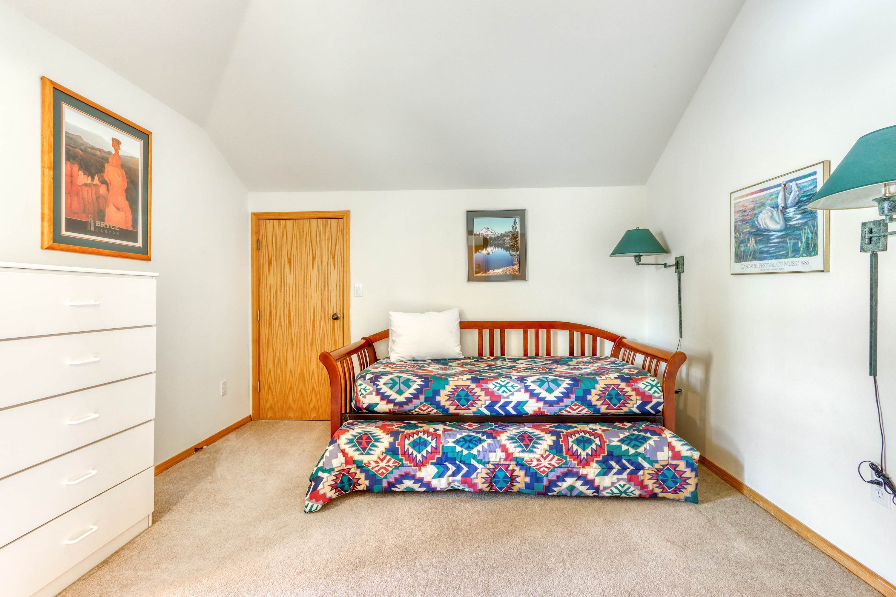 Une chambre à coucher avec un lit, une commode, une porte et des tableaux encadrés accrochés aux murs.