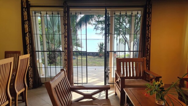 A room with a view of a beach, wooden furniture, and a potted plant. - Jugroop Beach House (Tombeau Bay)