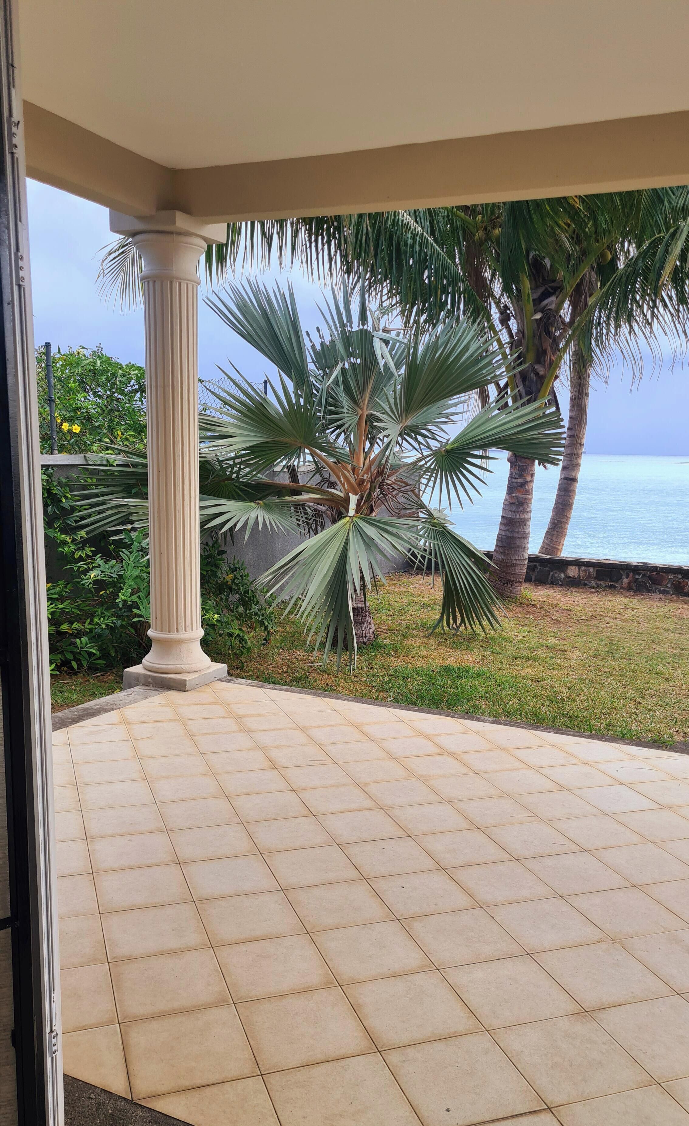 Um alpendre coberto com uma palmeira, vista para o mar e chão em mosaico.