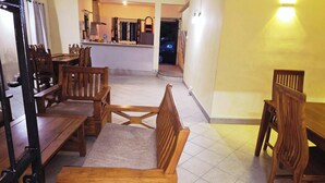 A dining area with wooden furniture, a kitchen in the background, and a yellow wall. - Jugroop Beach House (Tombeau Bay)