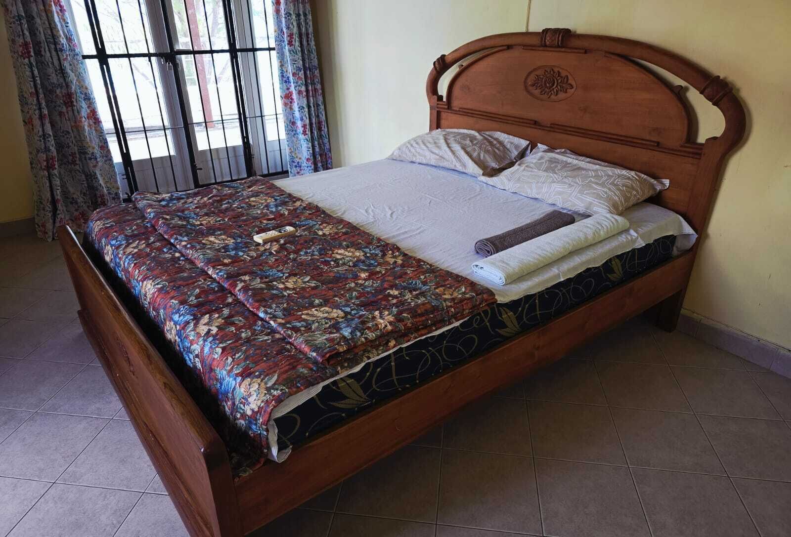 A wooden bed with a floral bedspread, a white pillow, and a rolled towel.