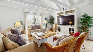Ein Wohnzimmer mit Sofa, Sessel, Couchtisch, Fernseher und Pflanzen.