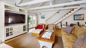 Ein geräumiger Wohnbereich mit einem großen Flachbildfernseher, Holzmöbeln, einer Treppe und Blick ins Freie.