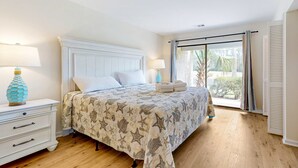 Une chambre à coucher avec un lit, des tables de chevet, une fenêtre avec des rideaux et une vue sur l’extérieur.