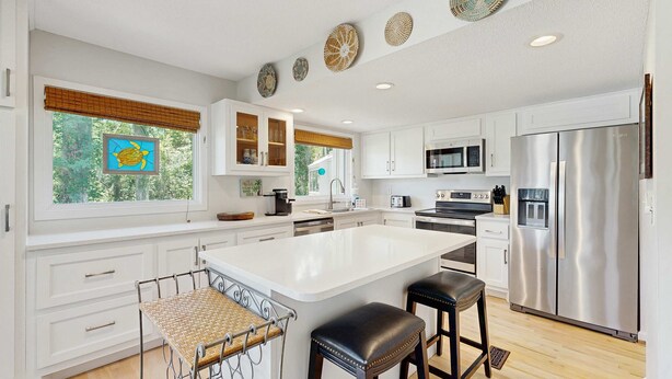 A modern kitchen with white cabinetry, a large island, stainless steel appliances, and decorative wall plates. - Home with patio, golf views, close to beach and restaurants (Edisto Beach)