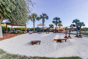 Ein Sandbereich im Freien mit Holzbank, Laube, Palmen und Spielplatz.