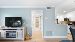 Ein modernes Wohnzimmer mit Flachbildfernseher, Kamin und Küchenbereich mit weißen Schränken und Geräten.