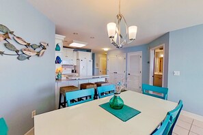 Un comedor con una mesa blanca, sillas color aguamarina, una araña y una decoración de peces en la pared.