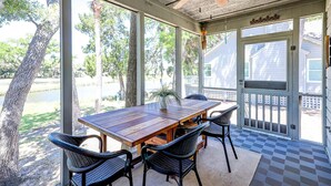 Une terrasse couverte avec une table et des chaises en bois, de grandes fenêtres et un ventilateur de plafond.