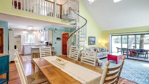 Un vaste espace dédié à la salle à manger, avec une table en bois, des chaises blanches et un escalier menant à un niveau supérieur.
