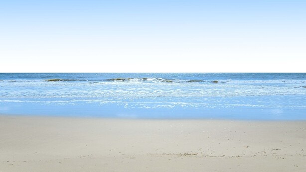 Ein Strand mit blauem Himmel und ruhiger See.