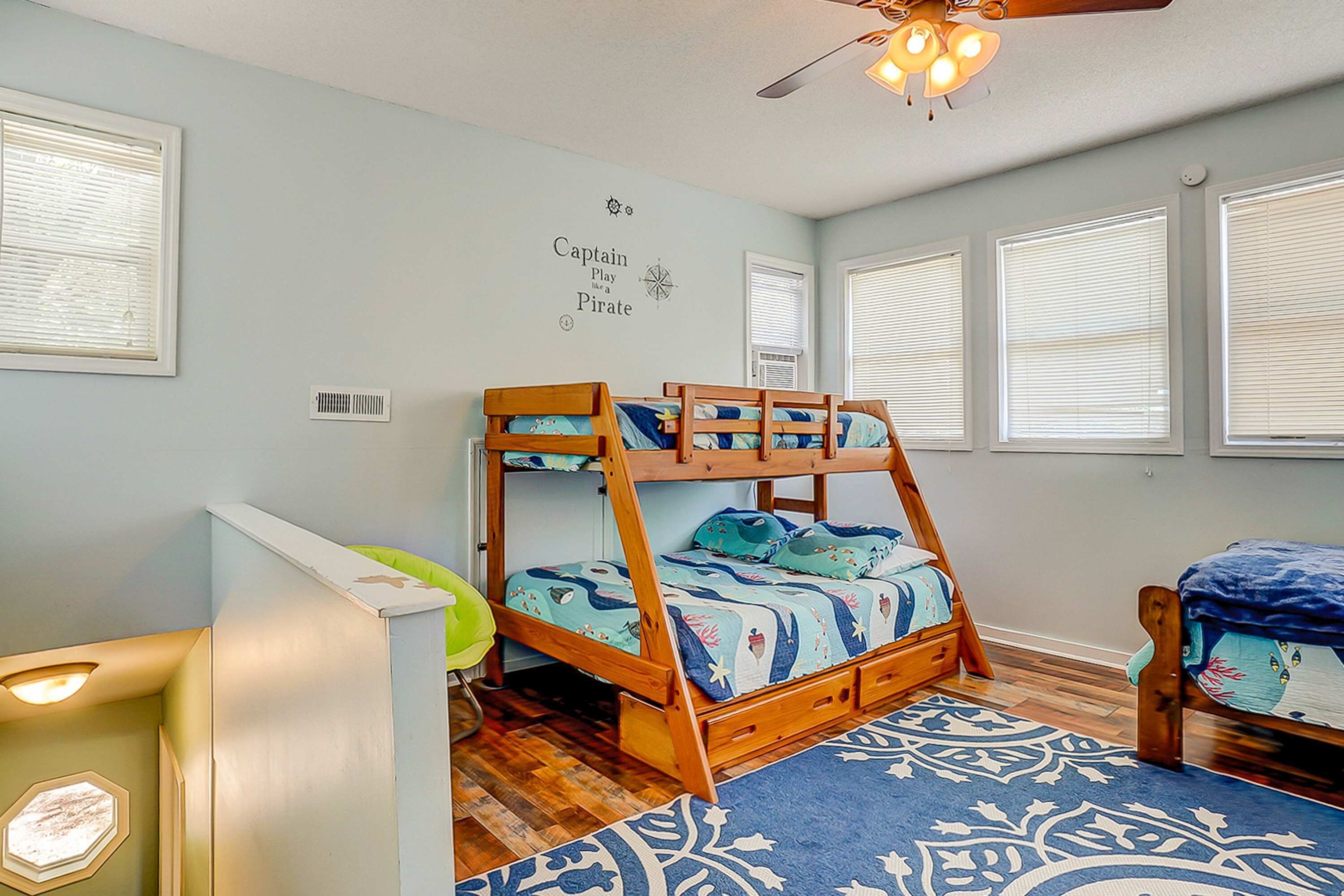 A bunk bed room with a ceiling fan, a desk, and a window with blinds.