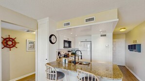 Una cocina con una isla central, taburetes de bar, una decoración con timón de barco y un reloj en la pared.