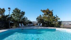 Una piscina con sillas de descanso, una valla y árboles al fondo.