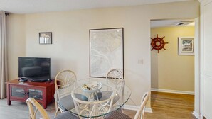 Una sala de estar con un televisor sobre un mueble, una mesa de vidrio con sillas, un mapa enmarcado y un adorno de timón.