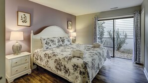 Un dormitorio con cama, mesitas de noche, ventana con cortinas y vistas al exterior.