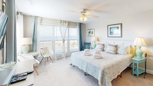 A bedroom with a bed, bedside tables, a ceiling fan, and a window with curtains. - Oceanfront house with ocean views & beach access - near dining & golf (Edisto Beach)