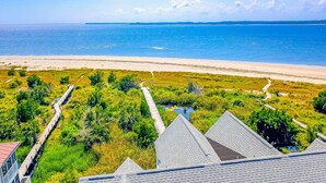 A coastal view with a beach, a wooden boardwalk, and a building with a sloped roof. - Oceanfront house with ocean views & beach access - near dining & golf (Edisto Beach)