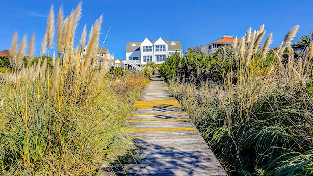 A pathway leading to a large house with a white exterior and multiple windows. - Oceanfront house with ocean views & beach access - near dining & golf (Edisto Beach)
