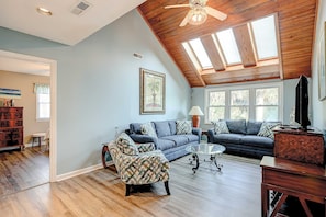 A spacious living room with a high ceiling, wooden beams, a large window, and a cozy seating area. - Newly Updated, Dog-Friendly Home w/ Screened Porch & WiFi - Walk to the Beach (Edisto Beach)