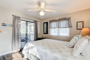 A bedroom with a bed, a ceiling fan, a window with curtains, a door leading to an outdoor area, and a wall-mounted lamp. - Newly Updated, Dog-Friendly Home w/ Screened Porch & WiFi - Walk to the Beach (Edisto Beach)