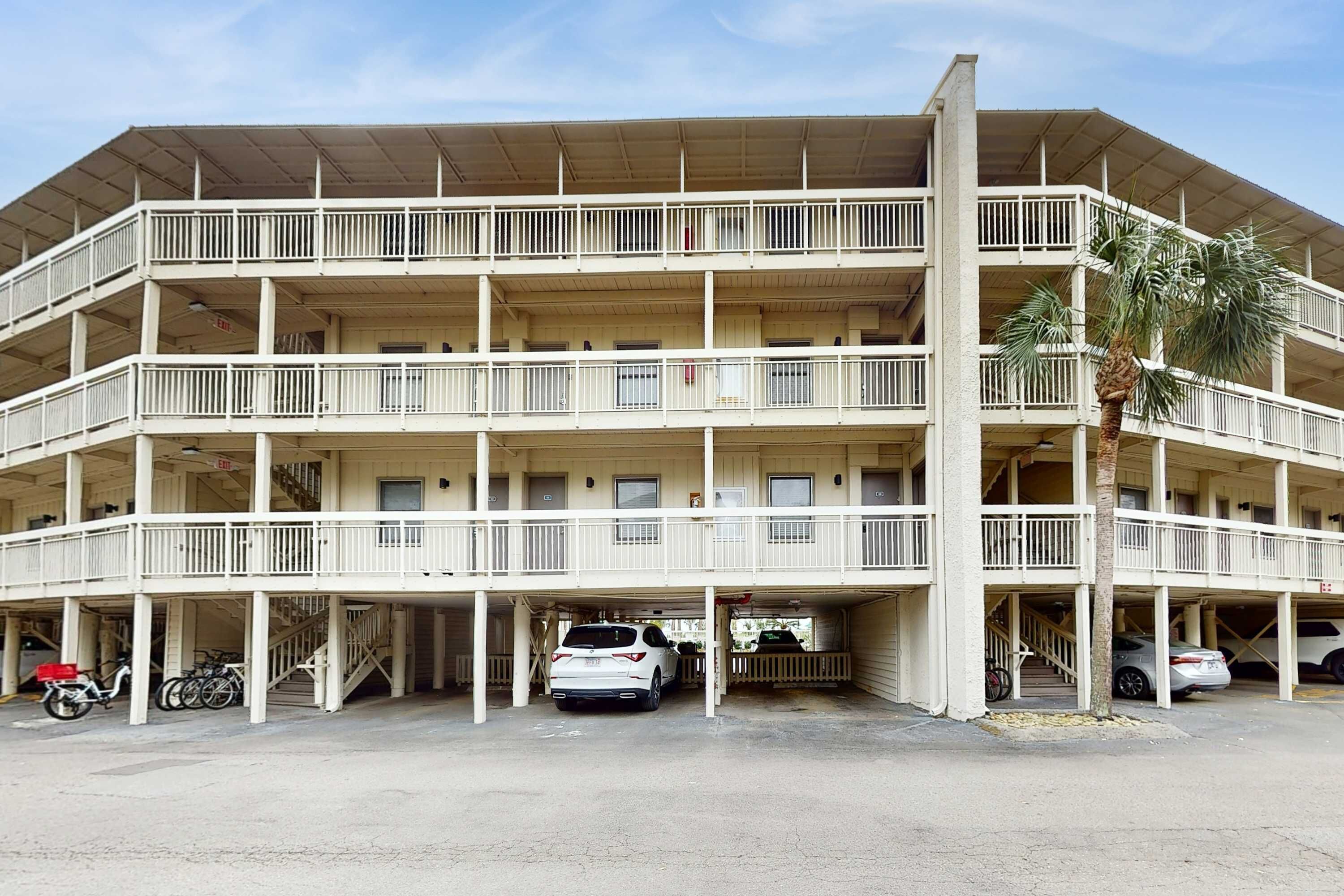 Un edificio de varios pisos con balcones, espacios de estacionamiento y una palmera.
