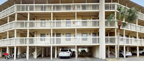Un edificio de varios pisos con balcones, espacios de estacionamiento y una palmera.