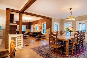 A spacious dining area with a wooden table and chairs, a patterned rug, and a chandelier. - 172 Acres Catskills Estate with Pool, Hot Tub, Sauna & Rustic Barn by the pond. (Long Eddy)