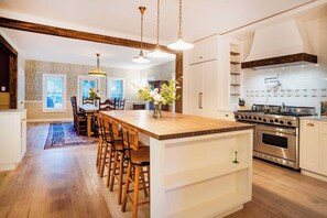 A modern kitchen with a central island, wooden chairs, pendant lights, and a large stove. - 172 Acres Catskills Estate with Pool, Hot Tub, Sauna & Rustic Barn by the pond. (Long Eddy)