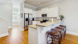 A kitchen with white cabinets, a stainless steel refrigerator, a microwave, a sink, and a bar area with stools.