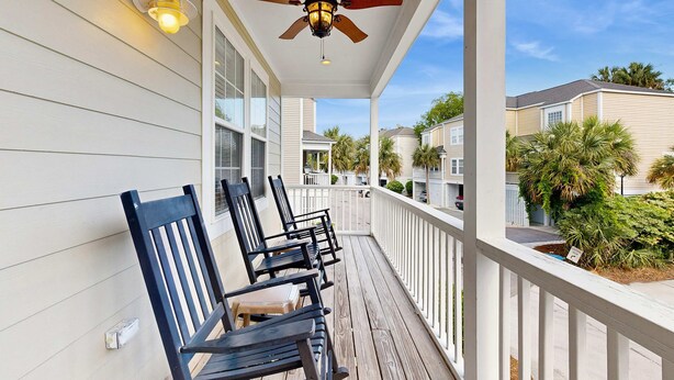 A covered porch with ceiling fans, outdoor seating, and a view of neighboring buildings and palm trees.