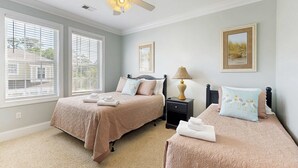 A bedroom with two beds, a ceiling fan, a nightstand with a lamp, and framed pictures on the wall.
