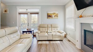 Ein Wohnzimmer mit einem beigen Sofa, einem Kamin, einem Fernseher und einem Gemälde an der Wand.