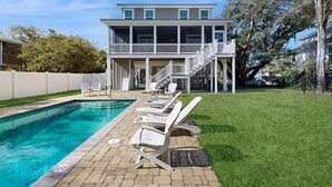 Ein zweistöckiges Haus mit Schwimmbad, Liegestühlen und einer überdachten Terrasse.