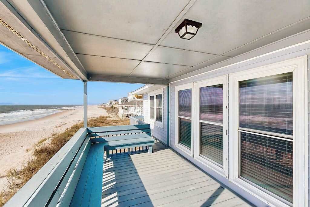 A covered porch with a view of the beach, a bench, and a door with a window.