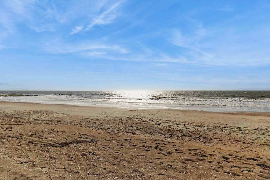 Ein Strand mit Fußspuren, blauem Himmel und ruhigem Wasser.