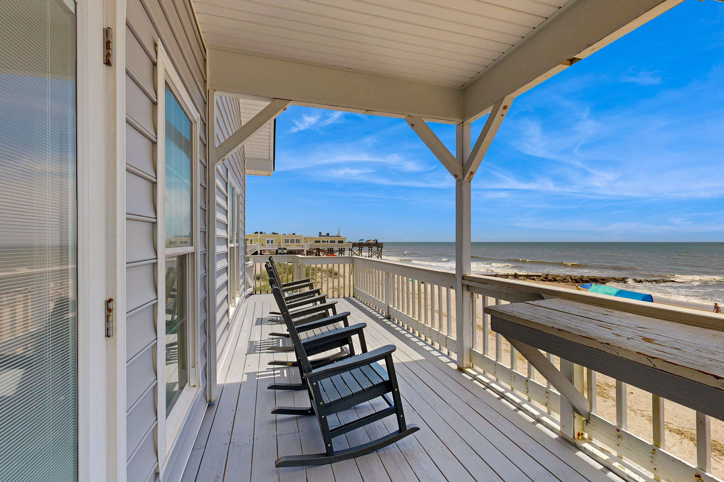 A covered deck with wooden benches, a railing, and a view of the beach and ocean.