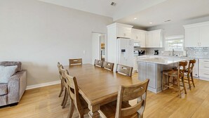 A modern kitchen with white cabinets, a wooden dining table, and a ceiling fan. - Newly renovated beachfront house w/Patio, Free WiFi, Private W/D, AC (Edisto Beach)
