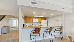 A modern kitchen with wooden cabinets, a microwave, a refrigerator, and a bar area with three bar stools. - Beautiful home with natural light, lagoon views - Community Hot tub & Pool (Edisto Beach)