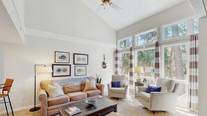 A living room with a sofa, armchairs, a coffee table, and a large window with curtains. - Beautiful home with natural light, lagoon views - Community Hot tub & Pool (Edisto Beach)